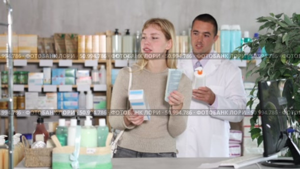 Girl studies composition of body lotion, man pharmacist in background. Стоковое видео, видеограф Яков Филимонов / Фотобанк Лори