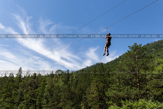 Girl tourist is going down the ropes - a bungee cable - from a mountain waterfall above the wooded gorge of the Kyngarga River. Extremely active summer holiday. Siberia. Buryatia. Arshan resort. Стоковое фото, фотограф Виктория Катьянова / Фотобанк Лори
