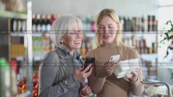 Girl with senior female relative in store scan QR code on yogurt label. In mobile app, buyer receive information about yogurt. They check manufacturer data in registry database of national agency. Стоковое видео, видеограф Яков Филимонов / Фотобанк Лори
