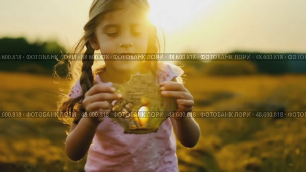 Golden Hour Discovery: Young Girl with Long Hair Holding a Mysterious Handcrafted Object in a Sunlit Field. Evocative scene for storytelling or childhood themes. Стоковое AI-видео, аниматор Данила Большаков / Фотобанк Лори