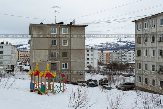 Город Магадан, Магаданская область, Россия. Вид на городской квартал и заснеженную детскую площадку во дворе. Множество серых панельных зданий. Холодная снежная погода. Повседневная жизнь в Сибири и на Дальнем Востоке России. (2018 год). Редакционное фото, фотограф Андрей Степанов / Фотобанк Лори