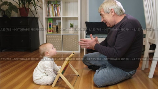 Grandfather playing with little baby. Caring granddad and cute toddler grandchild lying on warm floor together, having fun at home. Happy old senior man teach little grandson playing colorful blocks. Стоковое видео, видеограф Марина Демидюк / Фотобанк Лори