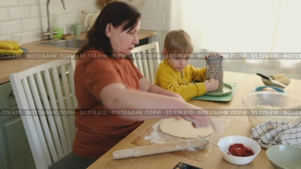 Grandma teaching grandson to make pizza dough. Happy Caucasian granny and grandchild making pizza in kitchen. Cute boy cooking together with grandmother. Family leisure. Multi generation family video. Стоковое видео, видеограф Марина Демидюк / Фотобанк Лори
