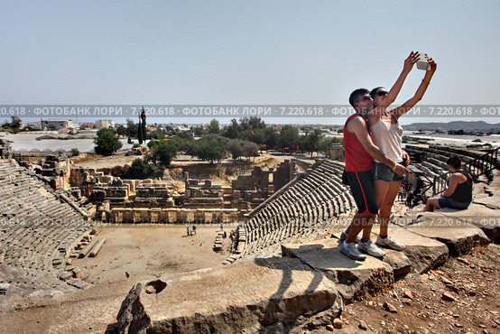 Greek theater in ancient town of Myra, Antalya region, Turkey Двое молодых туристов делают селфи на фоне древнего амфитеатра в городе Мира, Анталия Турция (2014 год). Редакционное фото, фотограф Владимир Григорьев / Фотобанк Лори