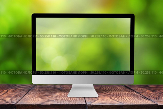 Green blurred computer monitor on a wooden table against the same natural background with bokeh, copy space. Working on nature, outside office concept.. Monitor with blurred screen and background. Стоковое фото, агентство Ingram Publishing / Фотобанк Лори