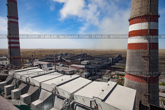 GRES-1 thermal power station. Grey raw coal bunkers on front. Smoke stacks both sides.Coal-harvesters in dust loading coal to electricity plant.Dry steppe,blue sky. Ekibastuz,Pavlodar reg.,Kazakhstan. Стоковое фото, фотограф Alexey Rezvykh / Фотобанк Лори
