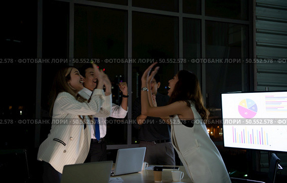 Group of broker international stock traders working actively at night in office, Everyone is congratulating the team on their success. Стоковое фото, агентство Ingram Publishing / Фотобанк Лори