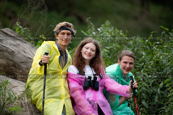 Group of friends in raincoats with backpacks on a hike in the forest, Prepare to hiking after the rain has stopped. Стоковое фото, агентство Ingram Publishing / Фотобанк Лори