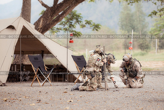 Group of soldiers in camouflage uniforms hold weapons in front of camp tent, Plan and prepare for combat training. Стоковое фото, агентство Ingram Publishing / Фотобанк Лори