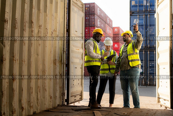 Group of workers in an empty container storage yard, The condition of the old container is being assessed to determine whether it requires maintenance for usage. Стоковое фото, агентство Ingram Publishing / Фотобанк Лори