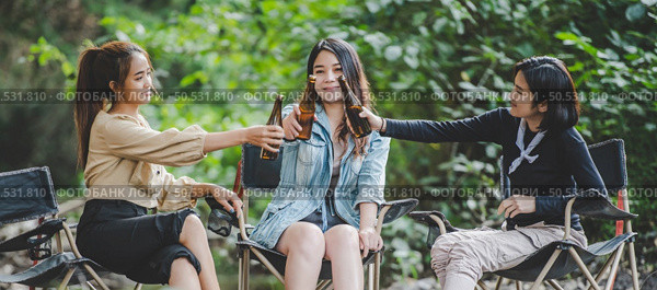 Group of young asian women drink beer in their chairs and soaked their feet in the stream while camping in the nature park, They are enjoy to talking and laugh fun together. Стоковое фото, агентство Ingram Publishing / Фотобанк Лори
