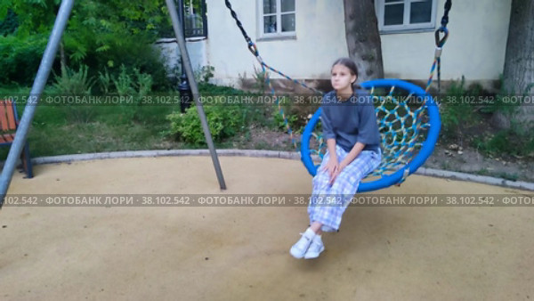 Грустная подросток девочка катается на круглой плетеной качели в городском парке. Подростковые проблемы, стресс и эмоции. Подростковая психология. Качели на детской площадке возле дома. Расстроенный ребенок. Замедленная съемка. Sad teen girl rides on round wicker swing in  city park. Teenage problems, stress and emotions. Adolescent psychology. Swing on the playground near the house. Frustrated child. Slow motion. Стоковое видео, видеограф Ирина / Фотобанк Лори