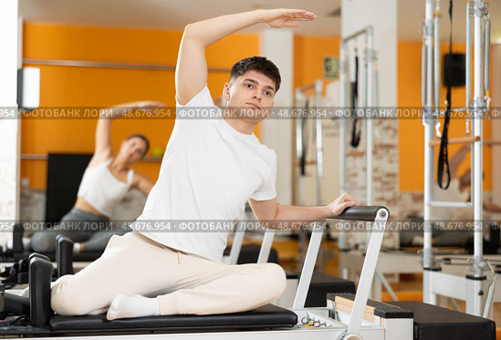 Guy doing side bend with arm extended on Pilates reformer. Стоковое фото, фотограф Яков Филимонов / Фотобанк Лори
