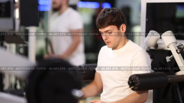 Guy in gym performs exercises for arm muscles using simulators and fitness center equipment. Стоковое видео, видеограф Яков Филимонов / Фотобанк Лори
