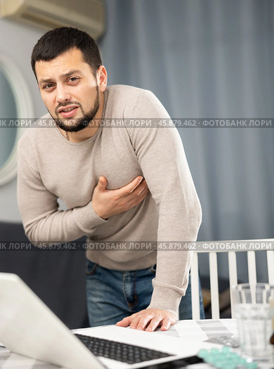 Guy suffering from chest pain standing near table with laptop at home. Стоковое фото, фотограф Яков Филимонов / Фотобанк Лори