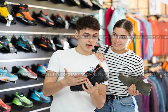 Guy with girlfriend, view specialized shoes in store, near showcase with summer trecking cross-shoes. Стоковое фото, фотограф Яков Филимонов / Фотобанк Лори
