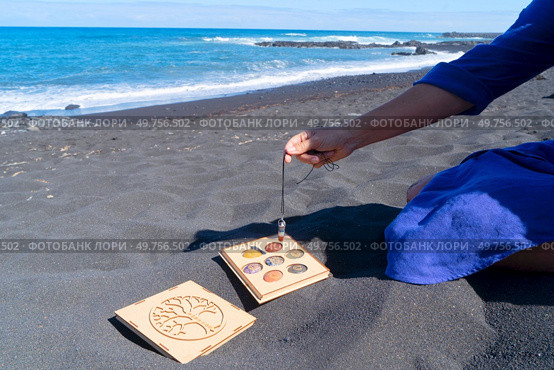 Hand holding pendulum with chakra healing crystals. Witchcraft, herbal medicine and healing, Magic healing Rock for Reiki Crystal Ritual, Witchcraft, spiritual esoteric practice. Healing crystals on black sand background. Стоковое фото, агентство Ingram Publishing / Фотобанк Лори