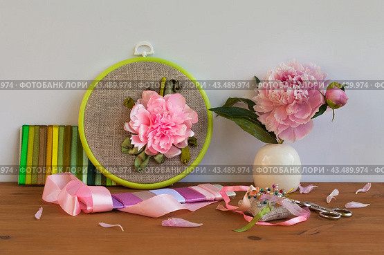 Handmade embroidery with satin ribbons of peony flower in hoop, bouquet of fresh peonies in vase on wooden table. Nearby is set of colorful satin ribbons, needles and scissors for work. Front view. DIY concept. Стоковое фото, фотограф Виктория Катьянова / Фотобанк Лори