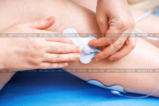 Hands attaching an electrode from an electrical muscle stimulator to a leg, demonstrating the application of EMS technology for muscle training and rehabilitation. Стоковое фото, фотограф Татьяна Степанищева / Фотобанк Лори