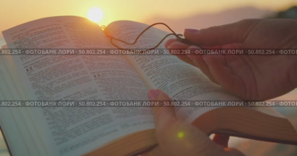 Hands hold open Bible book and wooden cross at beach during glowing sunset. Стоковое видео, видеограф Igor Tichonow / Фотобанк Лори