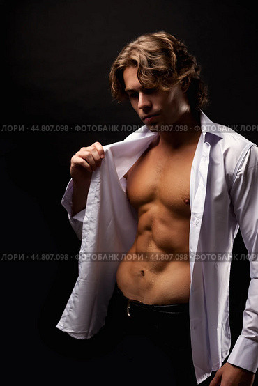 Handsome man advertising model in unbuttoned white shirt with abs muscle press posing in shadow at black studio shot. Portrait of stylish guy with perfect muscular sexy torso, pose. Copy ad text space. Стоковое фото, фотограф Aleksandr Golubev / Фотобанк Лори