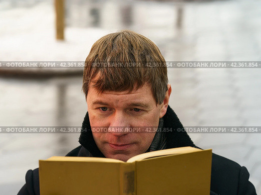 Handsome man in Moscow city center during coronavirus pandemic. New Year holidays. He sitting at the bench and reading the book in the public park. Стоковое фото, фотограф YuryKara / Фотобанк Лори