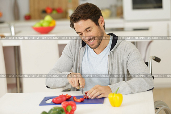 handsome man in wheelchair cuts veggetables. Стоковое фото, агентство Ingram Publishing / Фотобанк Лори