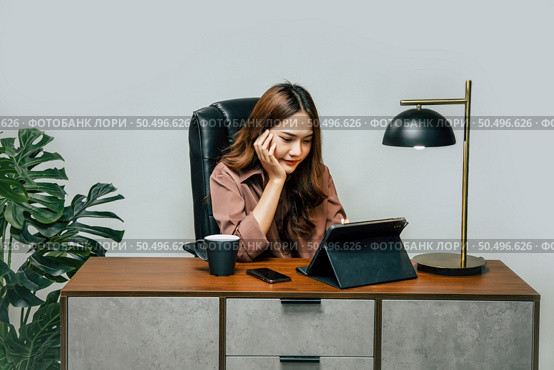 Happily Young asian woman with new normal, she Stay at home and works from home on digital tablet and use smartphone during self-isolation and quarantine covid-19 coronavirus outbreak. Стоковое фото, агентство Ingram Publishing / Фотобанк Лори