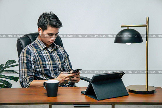 Happily Young handsome man with new normal, Stay at home and works from home on digital tablet and use smartphone during self-isolation and quarantine covid-19 coronavirus outbreak. Стоковое фото, агентство Ingram Publishing / Фотобанк Лори