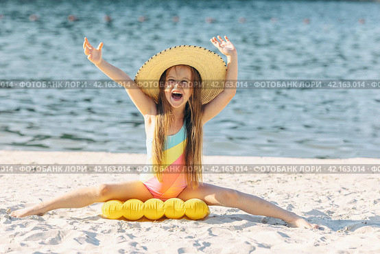 Happy cute smiling little girl in straw hat has fun on the sand on a beach in a swimsuit. Summer concept. Стоковое фото, фотограф Ирина Михайличенко / Фотобанк Лори