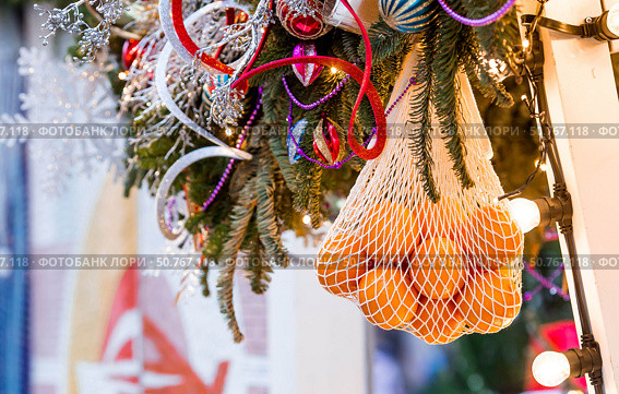Happy New Year 2026. Mandarins in a string bag and Christmas tree decorations on the streets of Moscow. The concept of preparing decorations and ornaments for Christmas. Стоковое фото, фотограф Photojuli / Фотобанк Лори