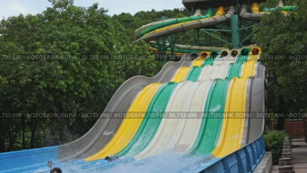 Happy people sliding down a water slide in aqua park, enjoying fun and summer activity. Excitement, playfulness, refreshing outdoor entertainment. Slow motion footage. Редакционное видео, видеограф Ирина Михайличенко / Фотобанк Лори