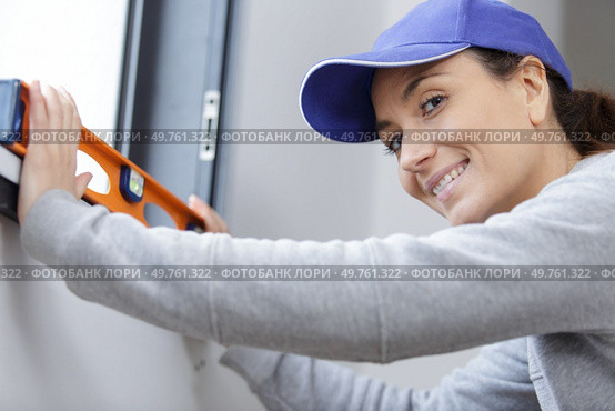 happy woman marks wall with bubble level. Стоковое фото, агентство Ingram Publishing / Фотобанк Лори
