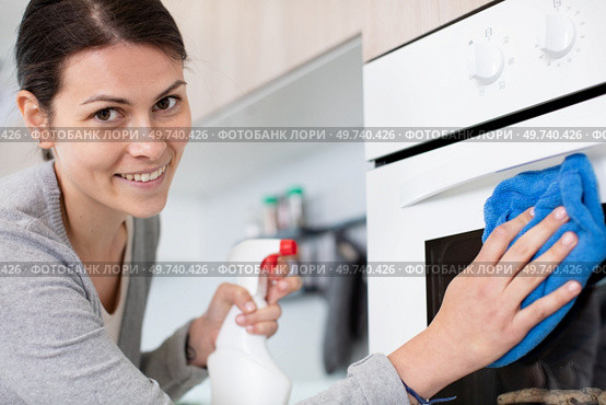 happy woman with bottle of spray cleanser cleaning domestic oven. Стоковое фото, агентство Ingram Publishing / Фотобанк Лори