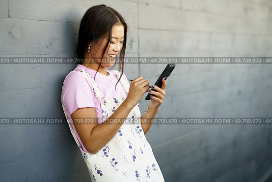 Happy Young Chinese woman using her smartphone with a pen or stylus, outdoors Asian female wearing casual clothes.. Happy Young Chinese woman using her smartphone with a pen or stylus, outdoors. Стоковое фото, агентство Ingram Publishing / Фотобанк Лори