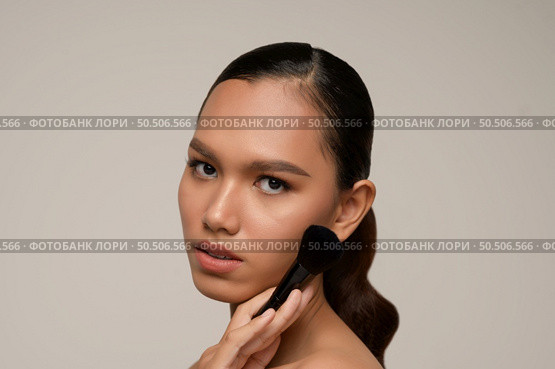 Head shot Portrait, Beauty portrait of asian attractive sensual young woman pose holding makeup blusher brush on her cheek isolated over gray background, copy space. Стоковое фото, агентство Ingram Publishing / Фотобанк Лори