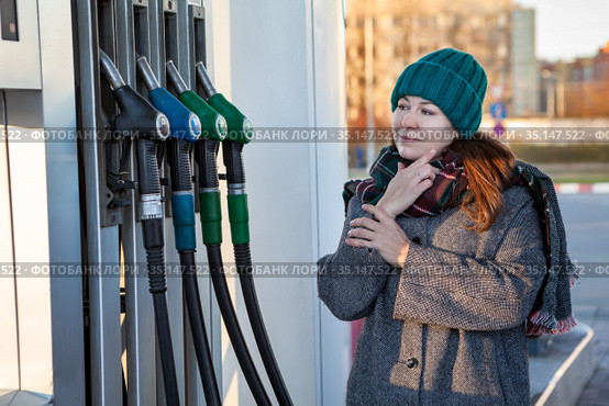 Hesitative woman deciding on type of fuel standing close to pump nozzles in petrol station. Стоковое фото, фотограф Кекяляйнен Андрей / Фотобанк Лори
