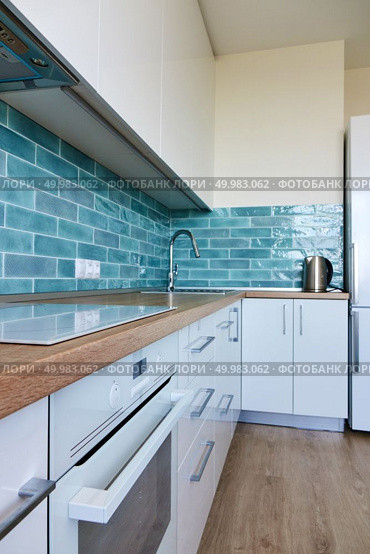 High glossy, white kitchen with blue tile, brown top, modern hob and oven. White glossy kitchen with modern appliances. Стоковое фото, агентство Ingram Publishing / Фотобанк Лори