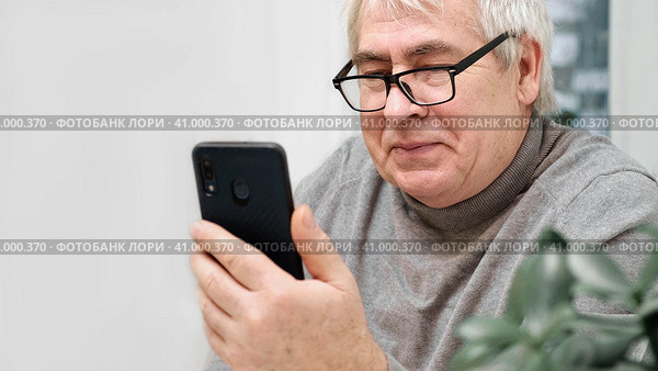 Hoary old man looking at web camera, holding phone, talking with children, wife online. Senior grandpa smiling chatting with friends, family via video call. Modern technologies and older generation. Стоковое фото, фотограф Марина Демидюк / Фотобанк Лори