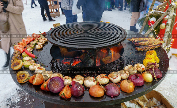 Holiday fair on the street in winter in the city. Cooking vegetables on the grill at the festivities (2024 год). Редакционное фото, фотограф Zima Nadezhda / Фотобанк Лори