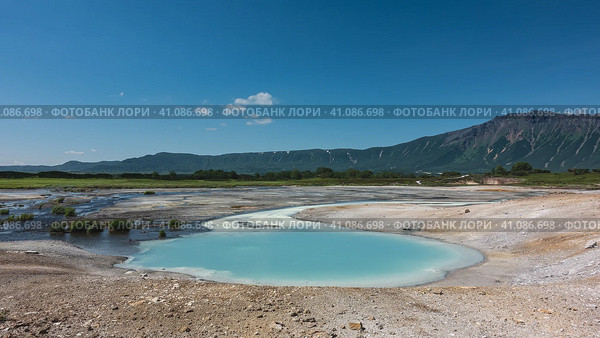 Hot natural springs flow into an amazing turquoise lake. Sulphurous deposits on the soil around. A picturesque mountain range against the blue sky. Kamchatka. The caldera of the extinct volcano Uzon. Стоковое фото, фотограф Вера Ивановна Кубарева / Фотобанк Лори