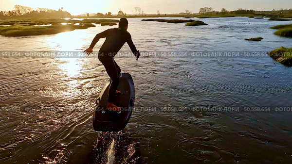 Hydrofoil rider gliding over the water with his board in one of the canals of the Ria de Aveiro in Portugal during sunset. Стоковое фото, агентство Ingram Publishing / Фотобанк Лори