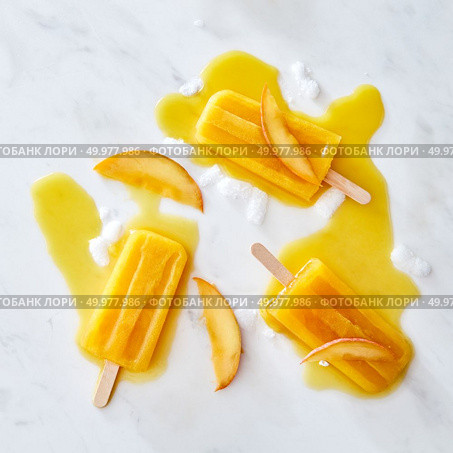 Ice cream lolly with fresh peach slices. Pattern of ice cream splashes and pieces of ice gray marble background with space for text. Flat lay. Appetizing melting ice cream on a stick with a pattern of splashes of ice cubes and pieces of peach on a gray marble background copy space. Flat lay. Стоковое фото, агентство Ingram Publishing / Фотобанк Лори