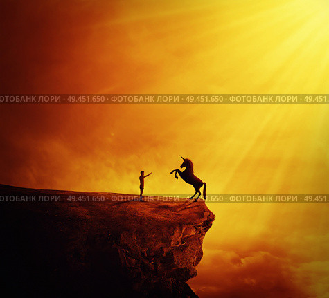 Idyllic view with a boy standing at the edge of a cliff chasm trying to tame a wild unicorn. Begining of a new friendship, fearless symbol. Стоковое фото, агентство Ingram Publishing / Фотобанк Лори
