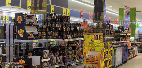 In a supermarket and shows shelves of products decorated in brightly coloured advertising packaging. In the foreground are boxes labelled Grilli Maistari, a range of sauces, seasonings and grilling products. Next to them are yellow boxes of Taffel snacks and chips. In the background are products from other brands, including Lay’s Sensations. The price tags on the top list the prices of various sauces, spices and products, starting from €1.49. The atmosphere of the store is typical of large supermarkets: bright lighting, saturated colours of the packaging and a wide variety of products. (2015 год). Редакционное фото, фотограф Анна Кривицкая / Фотобанк Лори