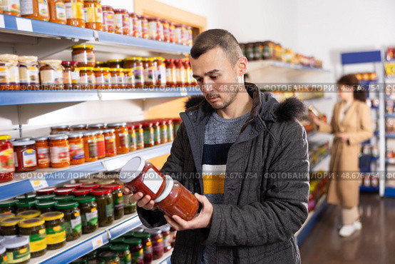 In Russian goods store, man choose jar of canned lecho. Стоковое фото, фотограф Яков Филимонов / Фотобанк Лори