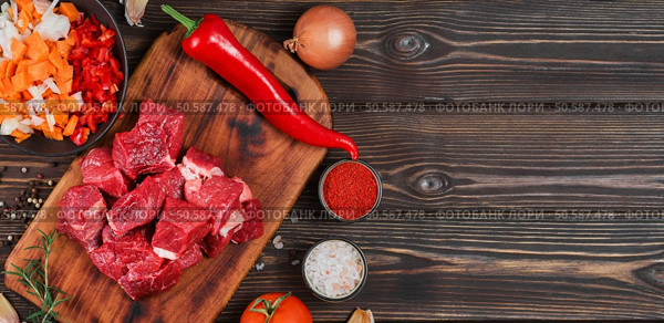 Ingredients for making goulash or stew, stew or gyuvech: top view of raw beef meat, herbs, spices, paprika, vegetables on a dark wooden background. Space for text, composition for flat lay. Стоковое фото, агентство Ingram Publishing / Фотобанк Лори