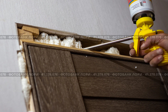 Installation of doors in the house. The master foams up the gaps between the door and the wall with polyurethane foam. Стоковое фото, фотограф Коханова Наталья / Фотобанк Лори