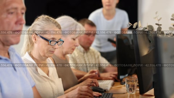Interested senior woman in glasses attending computer class, learning basics of digital technology under guidance of teacher standing in blurred background. Стоковое видео, видеограф Яков Филимонов / Фотобанк Лори