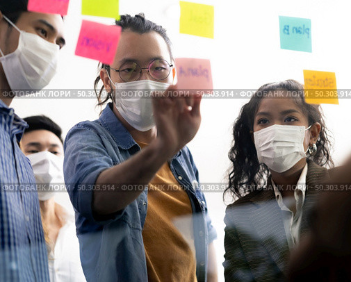 Interracial asian business team brainstorming idea at office meeting room after reopen due to coronavirus COVID-19 city lockdown. They wear face mask reduce risk to infection as new normal lifestyle. Стоковое фото, агентство Ingram Publishing / Фотобанк Лори